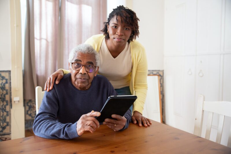 Woman standing and older man seated at a table with an ipad